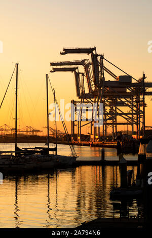 Puesta de sol sobre el horizonte de San Francisco y las grúas de elevación pesada del puerto de Oakland, Oakland, California Foto de stock