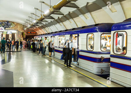 Los viajeros a bordo de un tren mientras dos limpiadores hembra barrer la plataforma en la estación de metro de coros, Tashknet Foto de stock