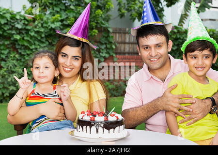 Felices los jóvenes padres y madres de familia y dos niños celebrando una fiesta de cumpleaños juntos en el patio de su casa Foto de stock