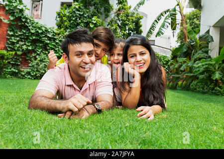 Feliz madre y padre de familia Two-Kids Lying-On-hierba relajante junto a divertirse disfrutando en el jardín de su casa Foto de stock