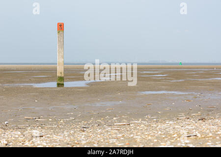La playa y el Mar del Norte durante la marea baja en Goeree-Overflakkee en los Países Bajos. Un solo palo de madera con la cabeza roja de pie en la arena, mientras ra Foto de stock