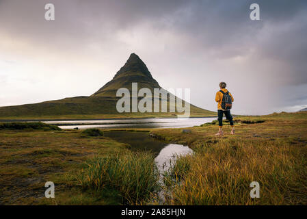 Excursionista joven con una mochila mira la montaña Kirkjufell en Islandia Foto de stock