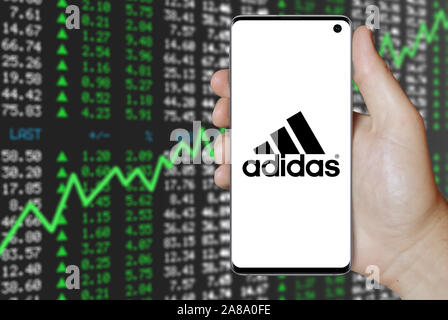 Logotipo de empresa pública Adidas muestra en un smartphone. Fondo de de valores. Crédito: Fotografía de stock - Alamy