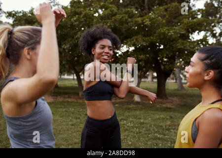 Grupo de colocar amigas multiétnica activa el calentamiento antes de una sesión de ejercicio en el parque