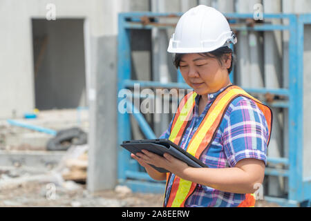 Las mujeres asiáticas, trabajador y ingeniero en sitio de construcción utilizando tablet para controlar la exactitud en los lugares antes de construir y casas.