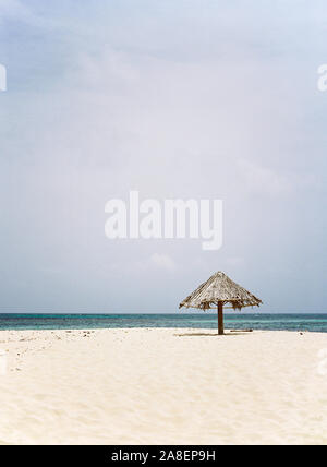 Un paraguas de frondas de palma descansando en la playa de la isla aislada de Mopion en San Vicente y las Granadinas. Foto de stock
