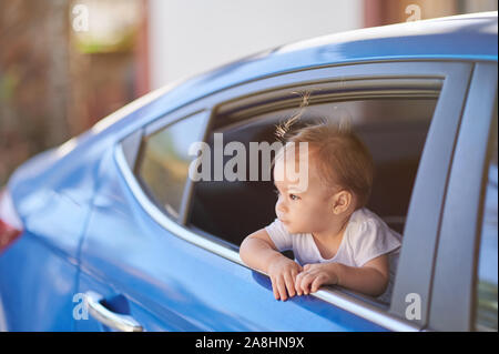 Cute baby girl mirar desde la ventana de coche azul