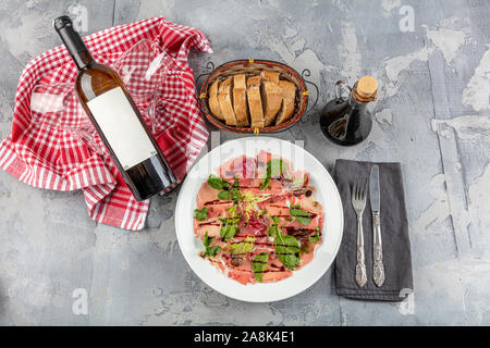 Carpaccio de Ternera aperitivo frío con vino, alcaparras y rúcula sobre placa blanca.vista desde arriba. Foto de stock