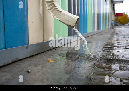 Desagüe con pavimento inundadas. El agua de lluvia que fluye desde un tubo de drenaje cerca. El clima de otoño.