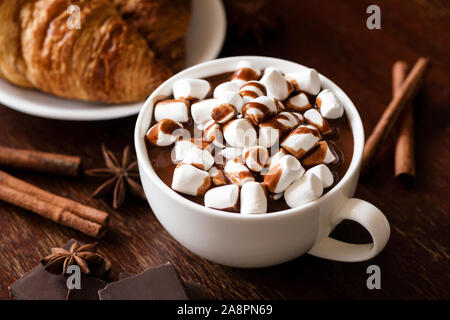Chocolate caliente con malvaviscos y canela en copa blanca en la mesa de madera