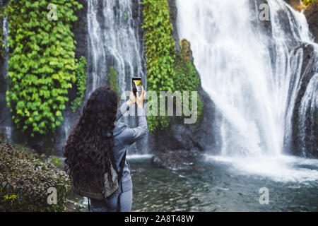 Mujer toma imagen de cascada Banyumala en Bali. Morena, pelo largo rizado mochila. Concepto de viaje.