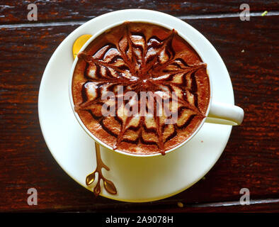Un cappuccino en una taza blanca en un platillo blanco con un bonito dibujo en la parte superior Foto de stock