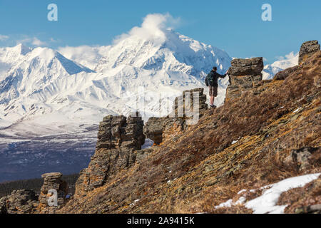 Un excursionista toma la vista del Monte Moffit y la Cordillera de Alaska mientras asciende Donnelly Dome; Alaska, Estados Unidos de América Foto de stock