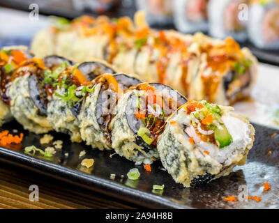 Placas con diversos tipos de expertamente cocida y rodajas de sushi con las especias y salsas picantes son mostrados en una mesa de comedor para disfrutar de la deliciosa y dietética Foto de stock
