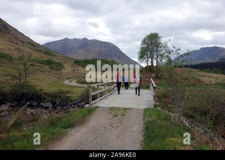 Tres hombres caminando sobre el puente de madera sobre el río 'Alt' en Glen Ceitlein Ceitlein hacia Ben Starav, Glen Etive, Scottish Highlands, Escocia, Reino Unido. Foto de stock