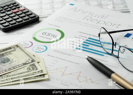Maqueta gráficos financieros informe hoja con pluma visible, calculadora, anteojos y billetes de dólar. Contabilidad, Negocios, Finanzas, impuestos y Office
