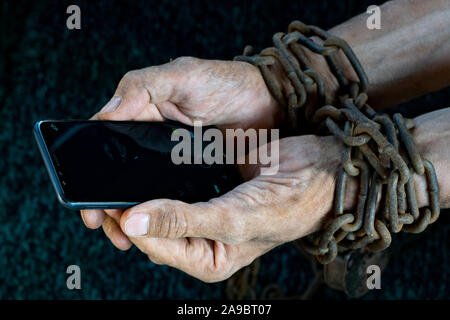 Hombre manos atadas con cadena metálica con candado sobre fondo oscuro sugiriendo internet o medios sociales adicción Foto de stock