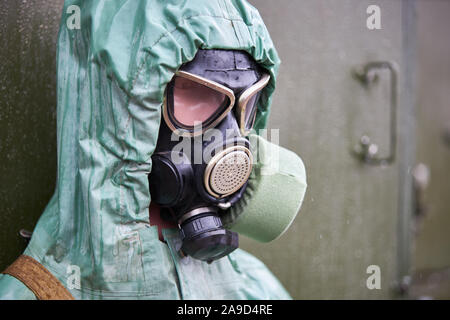 Maniqui vestido con traje de protección química de caucho verde y negro, máscara de gas cerca.