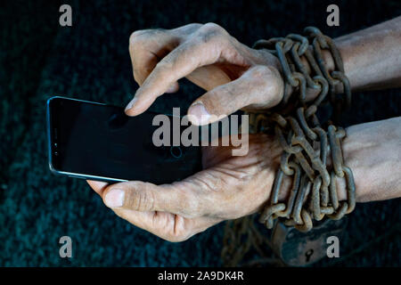 Hombre manos atadas con cadena metálica con candado sobre fondo oscuro sugiriendo internet o medios sociales adicción Foto de stock