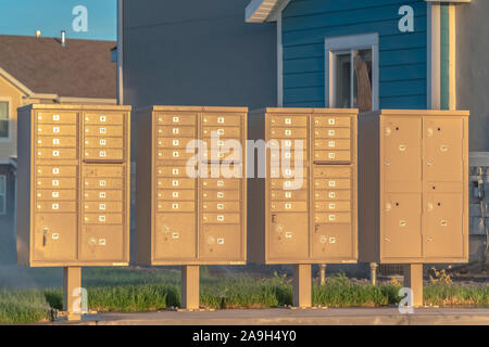 Fila de buzones con números y compartimentos junto a una carretera en un día soleado Foto de stock