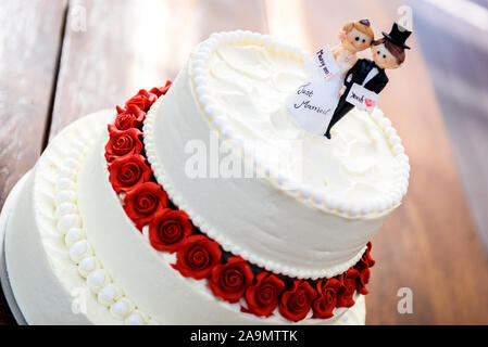Pastel de boda blanco con figuritas para el novio y la novia en la parte  superior. Hermoso blanco pastel de boda con rosas rojas en la tabla con el  esposo y la