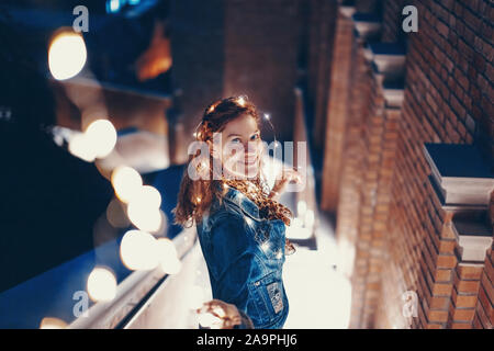 Mujer joven feliz jugando con las luces de hadas afuera en la ciudad Foto de stock