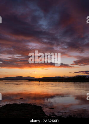 Rojo fuego, rosa, morado y naranja atardecer reflejado en calma, aún el agua a la boca del Loch Etive, Connel, Oban, Argyll and Bute, en Escocia, Reino Unido Foto de stock