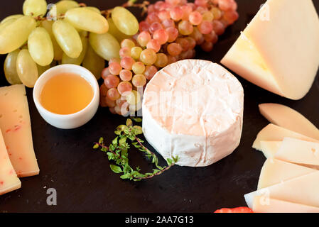 Plato de queso con queso azul, Brie, trufas, queso duro con uvas, higos, peras, miel, frutas y frutos de cáscara en el cuadro blanco. Vista desde arriba. Foto de stock