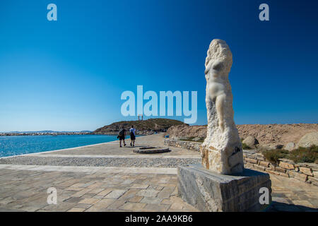 Naxos, Grecia - Julio 12, 2019: turistas caminando por la estatua de Ariadna, en el paseo marítimo que conduce a Portara, las ruinas del templo de Apolo en un día soleado Foto de stock