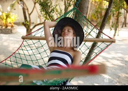 Mujer descansando en la hamaca en la playa tropical en la sombra, caliente día soleado