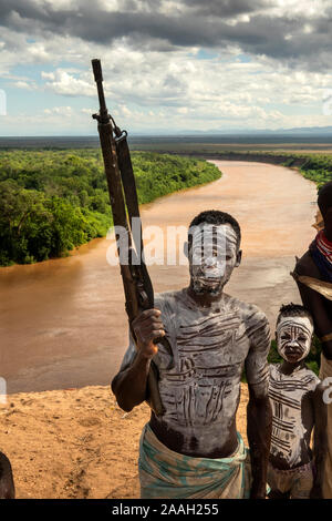 Etiopía, al sur de Omo, Kolcho village, Karo hombre tribal, decorado con barro blanco, con tornillo de un solo disparo de fusil de acción por encima del río Omo Foto de stock