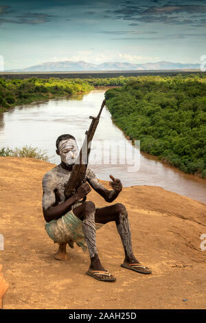 Etiopía, al sur de Omo, Kolcho village, Karo hombre tribal, decorado con barro blanco, con perno rifle de acción por encima del río Omo Foto de stock