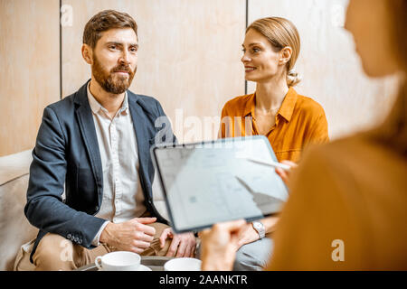 Pareja joven hablando con un gerente de ventas o agente inmobiliario, ofreciendo algunos productos con una tableta digital en la oficina