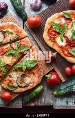 Vegetariana pizzas rústicas. Pizzas recién horneadas con berenjenas, pimientos y tomates en placas de roble con verduras crudas vista anterior