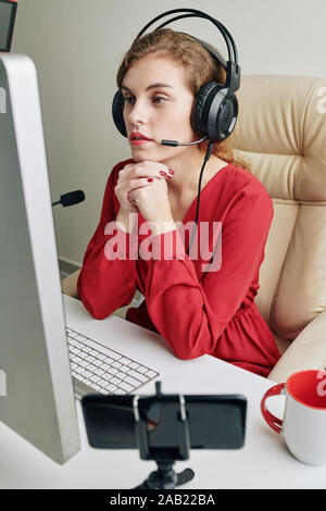 Blogger femenina en auriculares con micrófono viendo vídeos en la pantalla de ordenador y hacer comentarios