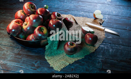 Las manzanas rojas frescas en un recipiente con media manzana y cuchillo sobre tela sobre madera.