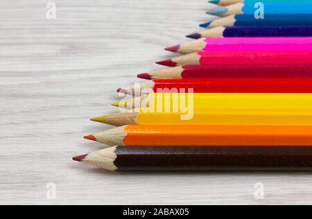 Vista en perspectiva de una serie de lápices de colores sobre un fondo de madera blanca Foto de stock