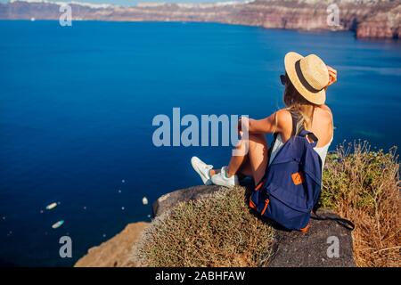 Viajero mujer sentada en el borde de la roca mirando desde Caldera Akrotiri, la isla de Santorini, Grecia. Turismo, Viajes Foto de stock
