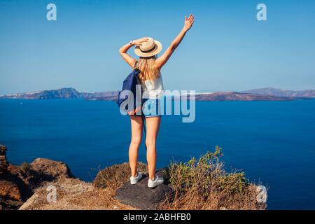 Mujer brazos levantados viajero sentirse feliz mirando desde Caldera Akrotiri, la isla de Santorini, Grecia. Turismo, Viajes Foto de stock