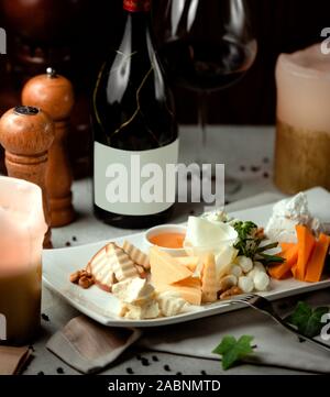 Diferentes tipos de lonchas de queso y una botella de vino tinto