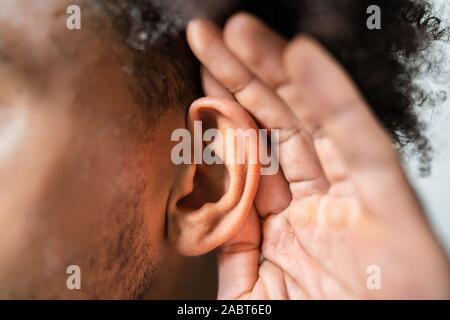Persona intentando escuchar con entregar la oreja Foto de stock