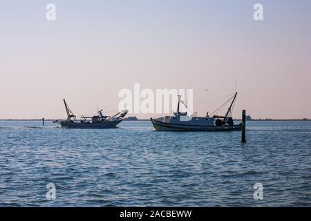 Dos barcos pesqueros pasan unos a otros en el canal estrecho que conduce a Marano Lagunare, Laguna di Marano, Friuli-Venezia Giulia, Italia Foto de stock