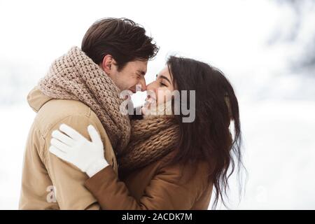 Dulce pareja frotando sus narices abrazando a pie en el bosque nevado