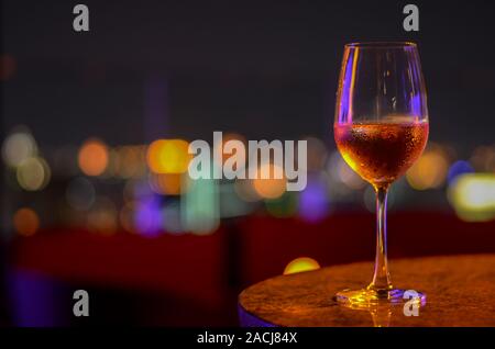 Un vaso de vino rosado con bokeh de luz a la ciudad de Bangkok y colorida luz desde el bar de la azotea.