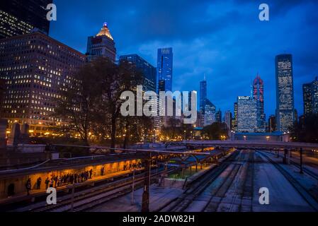 El horizonte de la ciudad de rascacielos iluminados en el centro de la zona de Chicago Loop y las líneas de ferrocarril y la gente esperando el tren, Chicago, Illinois, EE.UU. Foto de stock
