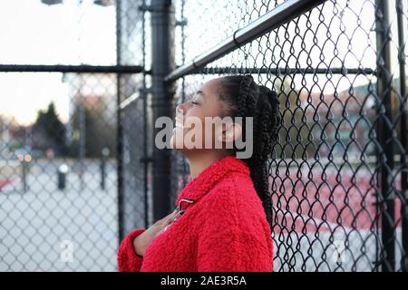 Una hermosa y alegre muchacha adolescente afroamericana de pie por una valla en una cancha de tenis