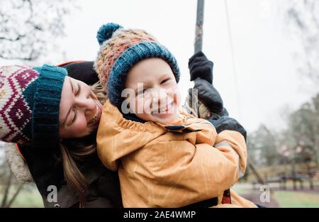 Retrato de una madre y su hijo jugando en un parque de la lluvia en invierno