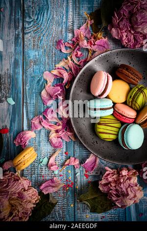 Gran foto de variadas y coloridas Macarons arreglado maravillosamente azul en la parte superior de la tabla de madera decorada con pétalos de flores púrpura Foto de stock