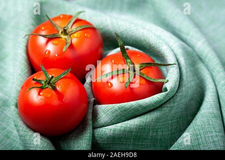 Tres tomate con gotas. Máxima profundidad de campo. Frescos rojos tomates maduros para su uso como ingredientes de cocina en primer plano con copyspace napki textiles Foto de stock