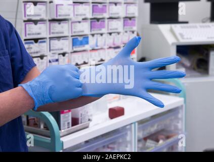 Un técnico de teatro se coloca un guante de cirugía en un hospital del NHS en quirófano. Mantener las cosas estériles es muy importante. Foto de stock